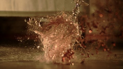 Floor view of a wineglass falling off a table and breaking into many pieces in super slow motion