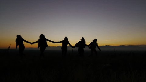 Silhouettes Of 5 Teen Girls Holding Hands Turn, Run Toward & Past Camera At Dusk