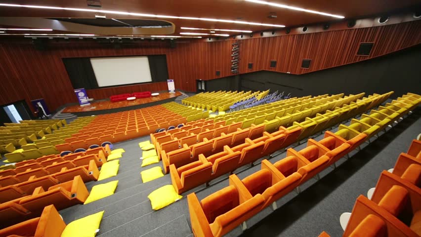 Empty big cinema hall with many rows of yellow and orange soft seats
