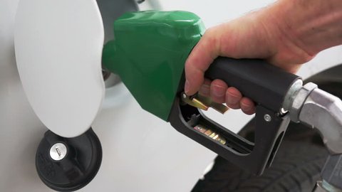 Close up shot of insertion of the nozzle and pumping gasoline into a white vehicle at the gas station.