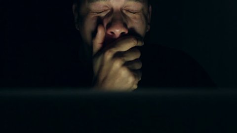 Tracking shot of a young mixed race man on his laptop at night looking very tired but pressing on with his work