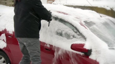 A man cleans snow off a parked car.
