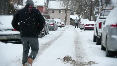 A single man walks down the middle of a street during a north eastern snow storm.