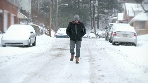 A single man walks down the middle of a street during a north eastern snow storm. Can be used as an abandoned, shelter-in-place, quarantine, social distancing concept.