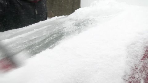 A man cleans snow off a parked car.