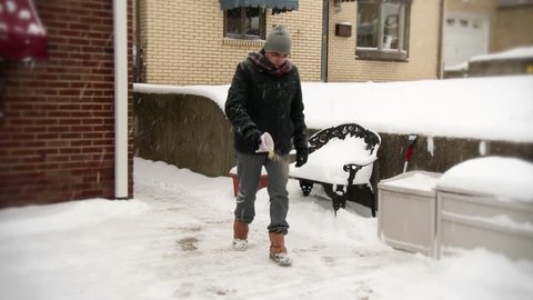 A man spreads salt on the sidewalk to melt the snow and ice.