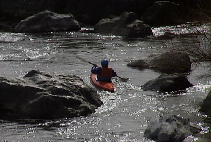 A kayak maneuvers between rocks, on a river.