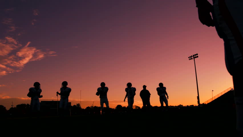 Football players warming up and having a catch as the sun sets.