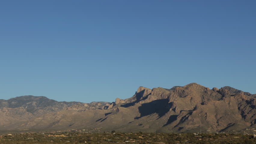 Timelapse: full moon rising over Santa Catalina mountains in Tucson, Arizona, glowing violet and blue at dusk with hills in silhouette as darkness falls. Oro Valley and Tucson visible in foreground.