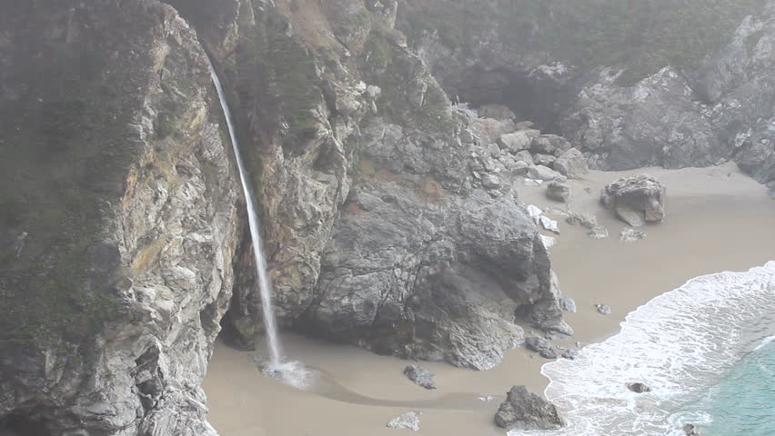 McWay Falls waterfall and breaking waves on a foggy day by the Pacific Ocean at Julia Pfeiffer Burns State Park on the California coast near Big Sur