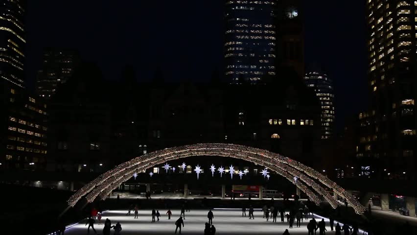 people ice skating at night in Nathan Phillips Square in Toronto