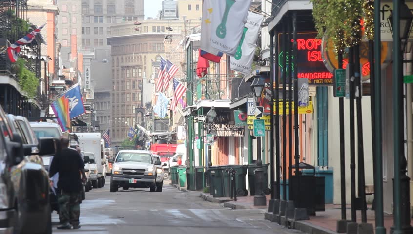 Truck drives down flag filled Bourbon Street with downtown in distance.