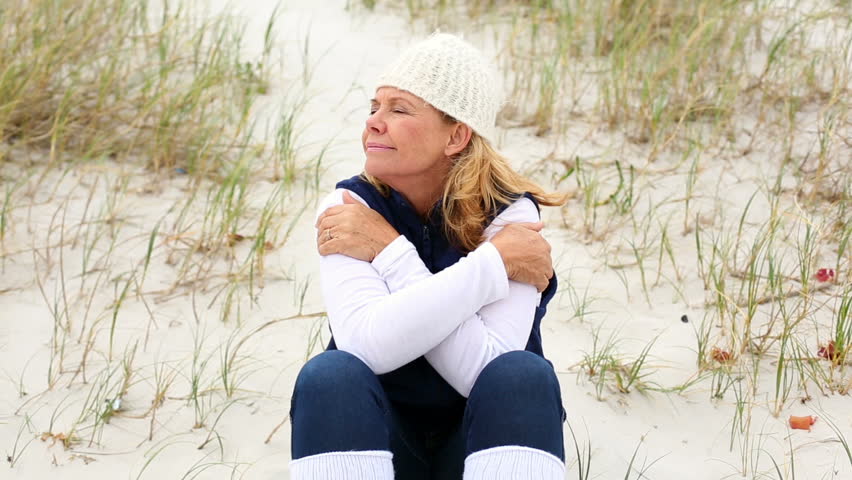 Retired woman sitting on the beach on a windy day