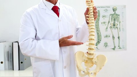 Doctor explaining skeleton model to camera in his office at the hospital