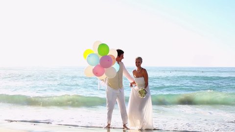 Newlyweds laughing and playing with balloons on the beach on their wedding day