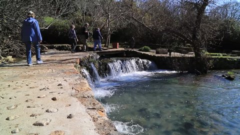 Tourists Walking Across the Bridge Over a Small Waterfall