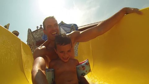 Attractive athletic and healthy father going down a bright colored water slide with his young son and a clear beautiful Summer afternoon. 