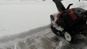 Man using a snow blower to clear out a driveway during a winter storm