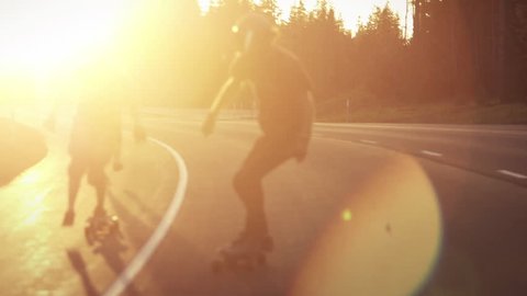 Skateboarders bomb hill during sunset in slowmotion