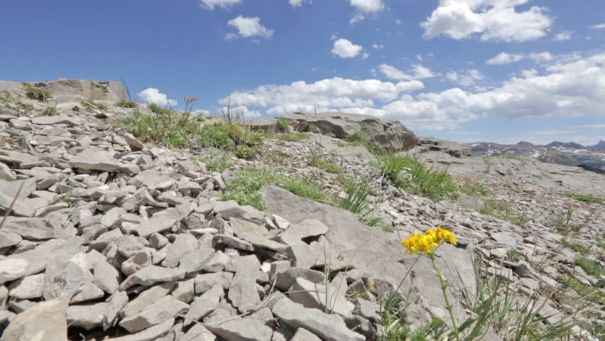 Two mountain bikers cross rocky ridge with Teton Mountains, ID in background tilt