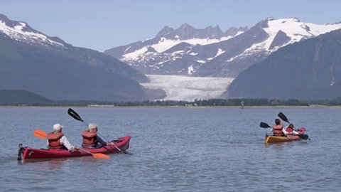 Three pairs of kayakers kayak towards snow covered mountains in Juneau, AK