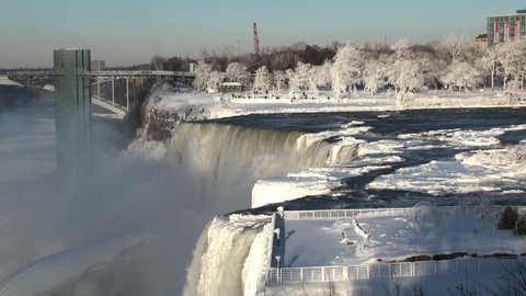 Classic winter portrait of the American Falls in Niagara Falls, NY. Ice covered trees caused by the mist are visible in the bright sun.