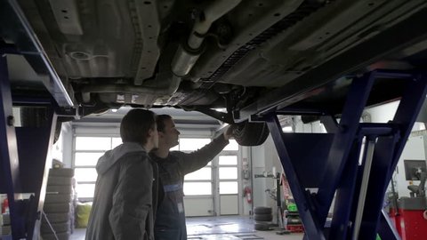 Mechanic and the car owner stand under the car and debate the issues