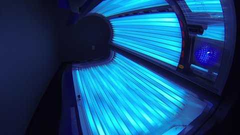 Bright tanning bed turned on. Smooth moving shot across the length of the brightly lit bed in slow motion.