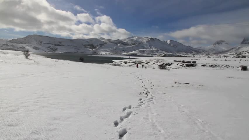 Trail of footprints in snow with two staff at the bottom next to a reservoir 