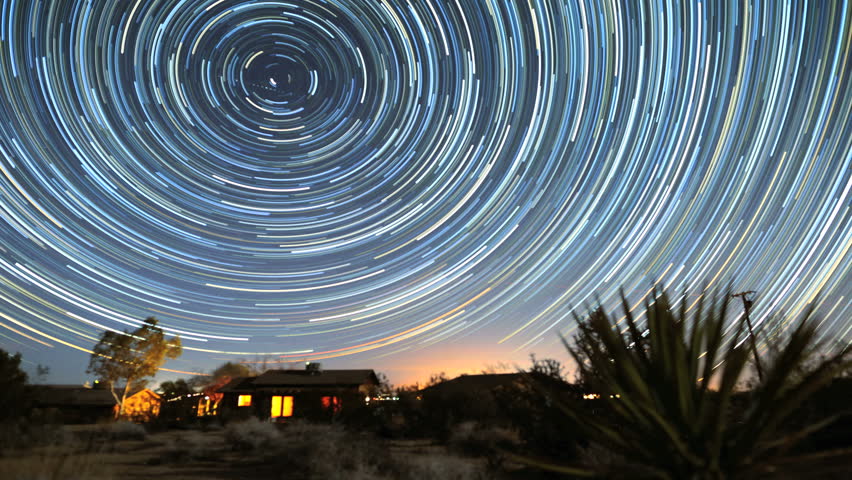 Amazing circle star trails time-lapse galaxy night sky over cabin as sun rises in Joshua Tree desert in California. 