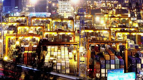 Containers Port Timelapse at Night. Hong Kong. Tight Shot. Cargo containers loading activities in cargo terminal.  Busy traffic across the main road at rush hour. Corporate buildings at the back.