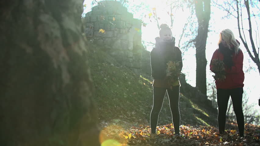 Two women throw leaves into the air shot from a far in slow motion