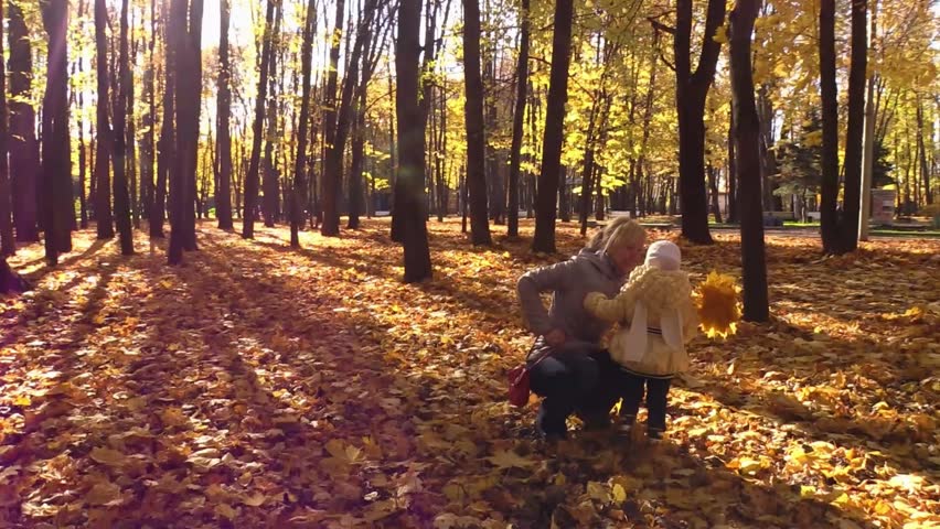 Mom and daughter play on the yellow leaves in sunny autumn park. Slow motion.