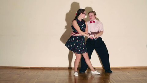 Girl and man in bow-tie dance boogie-woogie near wall in room. Shadows move at wall