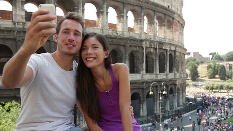 Tourist couple on travel taking selfie self-portrait pictures by Coliseum in Rome. Happy young romantic couple traveling in Italy, Europe taking photo with smartphone camera in front of Colosseum.