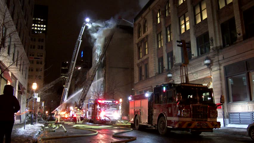 MONTREAL, QC - 1/2014 - 4K 60fps - Fire ladders attacking building fire. Wide angle shot of trucks and ladders spraying water on a building fire with smoke showing in old architecture style city setup