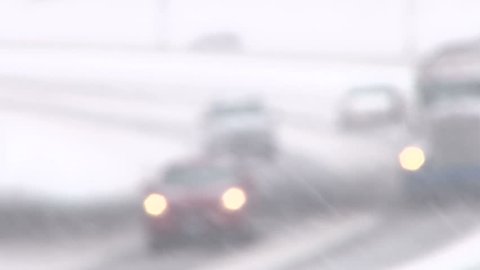 Rack focus traffic driving along freeway during heavy snow storm.