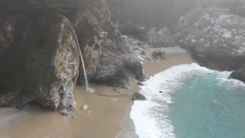 McWay Falls waterfall and breaking waves on a foggy day by the Pacific Ocean at Julia Pfeiffer Burns State Park on the California coast near Big Sur