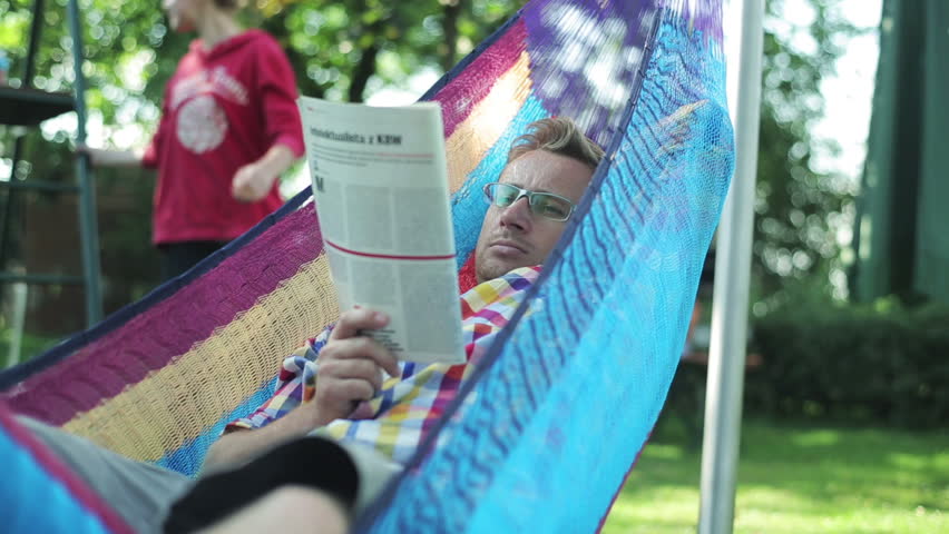 man reading the newspaper and lying in a hammock
