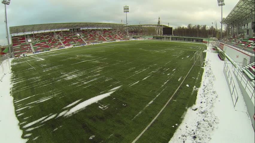 Soccer stadiums with empty tribunes and grass field covered by snow at winter day
