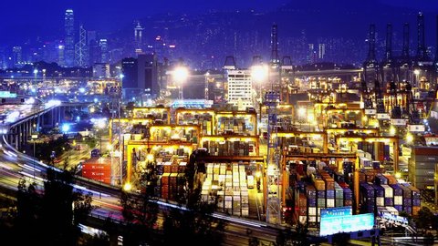 Containers Port Timelapse at Night. 4K Hong Kong. Tight Static Shot. Cargo containers loading activities in cargo terminal. Office buildings at the back. Busy traffic on the main road at rush hour. 