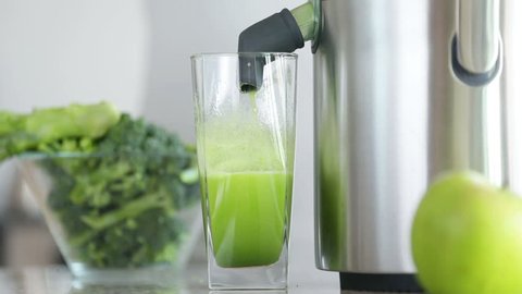Juicer making green broccoli vegetable juice. Close up of Juicing machine and green juice glass getting full and hand removing glass.