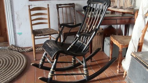 The black old rocking chair there are three chairs at the back and a small boat decor on the table