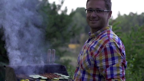 Smiling man grilling on an outdoor barbecue, slow motion shot at 120fps
