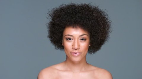 Shocked beautiful African American woman with a frizzy afro hairdo and bare shoulders standing with wide eyes and her mouth open in surprise