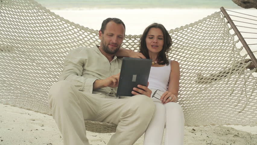 Couple on hammock chatting on tablet computer
