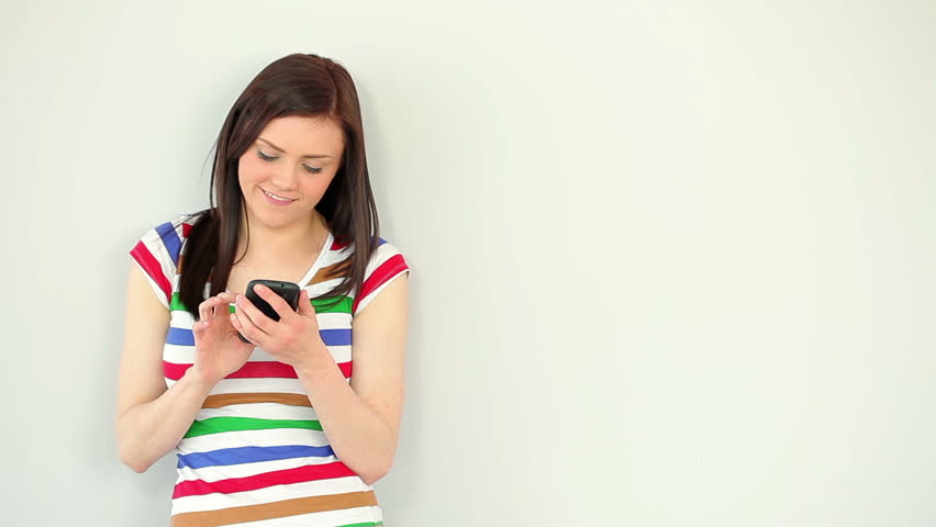 Happy young woman texting on her phone against a white wall