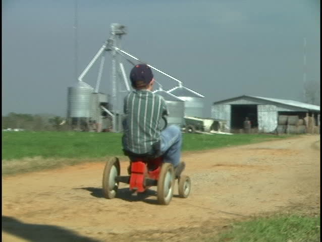 Rural farm boy (approximately 8 yrs. old) with a tractor pedal toy heading to the barn.