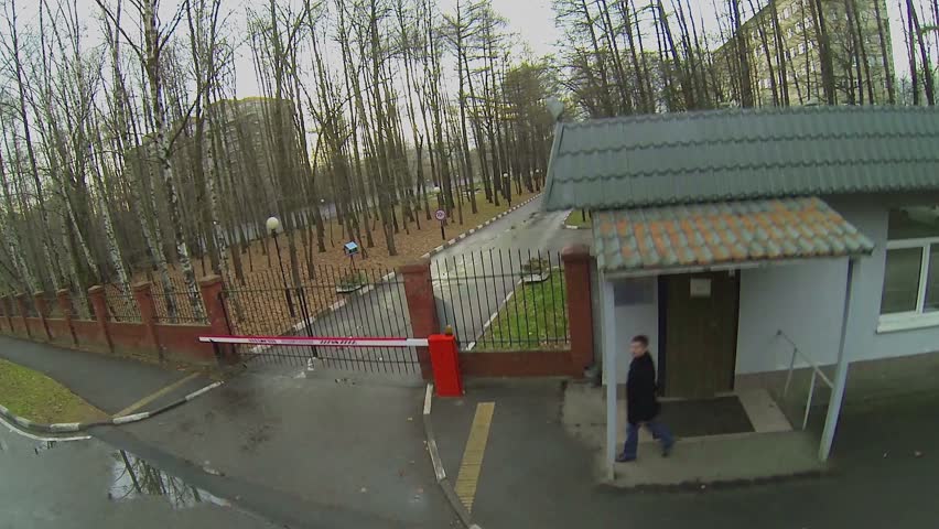 Man walk near gate and edifice of control post at autumn evening in park