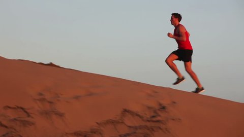 Runner man running up a hill sand dune in desert. Fit athletic male fitness model training. Sport in amazing extreme desert landscape nature at sunset with jogging male athlete.